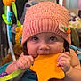 baby, child, pink_hat, knitted_hat, orange_toy, star_shaped_toy, activity_center, blue, purple, green, indoor, cute, smiling, playing, infant, person, closeup, face, hands, teething_toy