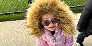 Madison is registered to the contest to win money with this photo: backpack, casual_clothing, chain_link_fence, child, colorful_shoes, concrete, daylight, fur_hood, green_turf, happy, hooded_jacket, outdoor, patterned_leggings, person, playful, smiling, sunglasses, urban, winter_clothing, young_child