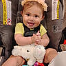 baby, child, infant, smiling, happy, flower_crown, car_seat, seatbelt, bunny, stuffed_animal, toy, colorful_toys, portrait, indoors, sitting, safe, brown_hair, yellow_shirt, close_up, adorable