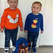 Mylan Luciano a rejoint le concours — aidez-le/la à gagner de superbes lots ! backpack, blue_sweater, boy, casual_clothing, child, cute, expression, floor, hair, indoor, jeans, orange_sweater, person, playful, portrait, smile, sneakers, standing, two_kids, wall