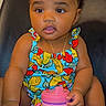 toddler, child, baby, sitting, colorful_clothing, hair_bows, sippy_cup, fruit_pattern, curious, indoors, portrait, cute, small_hands, necklace, black_hair, chair, bright_eyes, skin, face, expression
