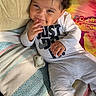 baby, child, curly_hair, onesie, smile, lying_down, blanket, colorful, cheeky, indoors, couch, cozy, cute, happy, infant, person, playful, relaxed, soft_toys, sunlight