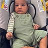 baby, car_seat, child, closeup, clothing, cute, expression, face, feet, green_overalls, hands, indoor, infant, person, portrait, seated, skin, soft_cushion, striped_shirt, warning_label