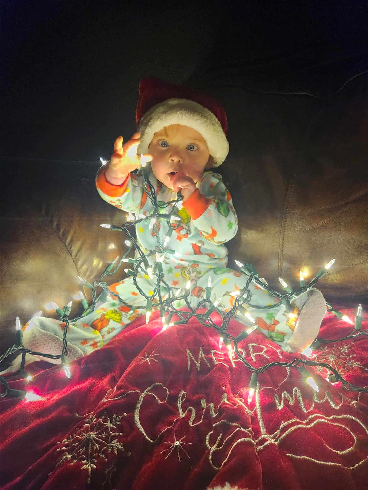 Blake joined the competition — help win amazing prizes! baby, child, christmas_lights, santa_hat, pajamas, couch, blanket, holiday, festive, indoors, glowing, cute, curious, face, person, bright, decor, celebration, winter, cozy