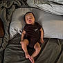 baby, sleeping, bed, pillow, blanket, onesie, black_clothing, person, infant, rest, indoor, soft, peaceful, cute, skin, foot, hand, face, young_child, relaxation
