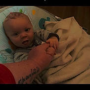 Bentley joined the competition — help win amazing prizes! adult_hand, baby, black_border, blanket, candid, child, cozy, face, home, indoor, infant, looking_at_camera, open_mouth, patterned_seat, portrait, sitting, tattoo, text_overlay, warm_lighting, wide_eyed