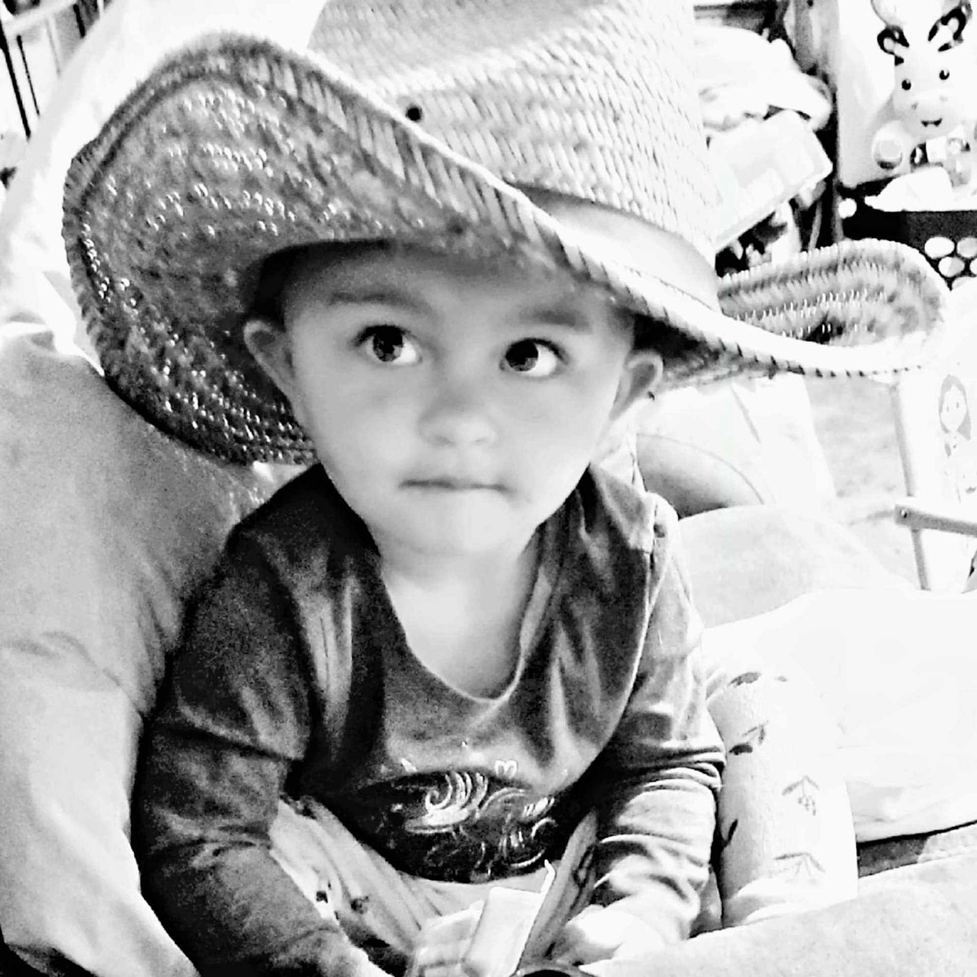 Nicci is registered to the contest to win money with this photo: black_and_white, casual, child, clothing, couch, cowboy_hat, curious, cushion, eyes, face, hat, home, indoor, person, portrait, sitting, smile, toddler, toy, young_child