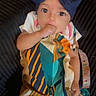 Ariyah joined the competition — help win amazing prizes! baby, infant, child, portrait, sitting, indoors, couch, cushion, bow, headband, colorful_clothing, dress, fashion, wide_eyed, smiling, hand_in_mouth, pacifier, baby_toy, seated, photography