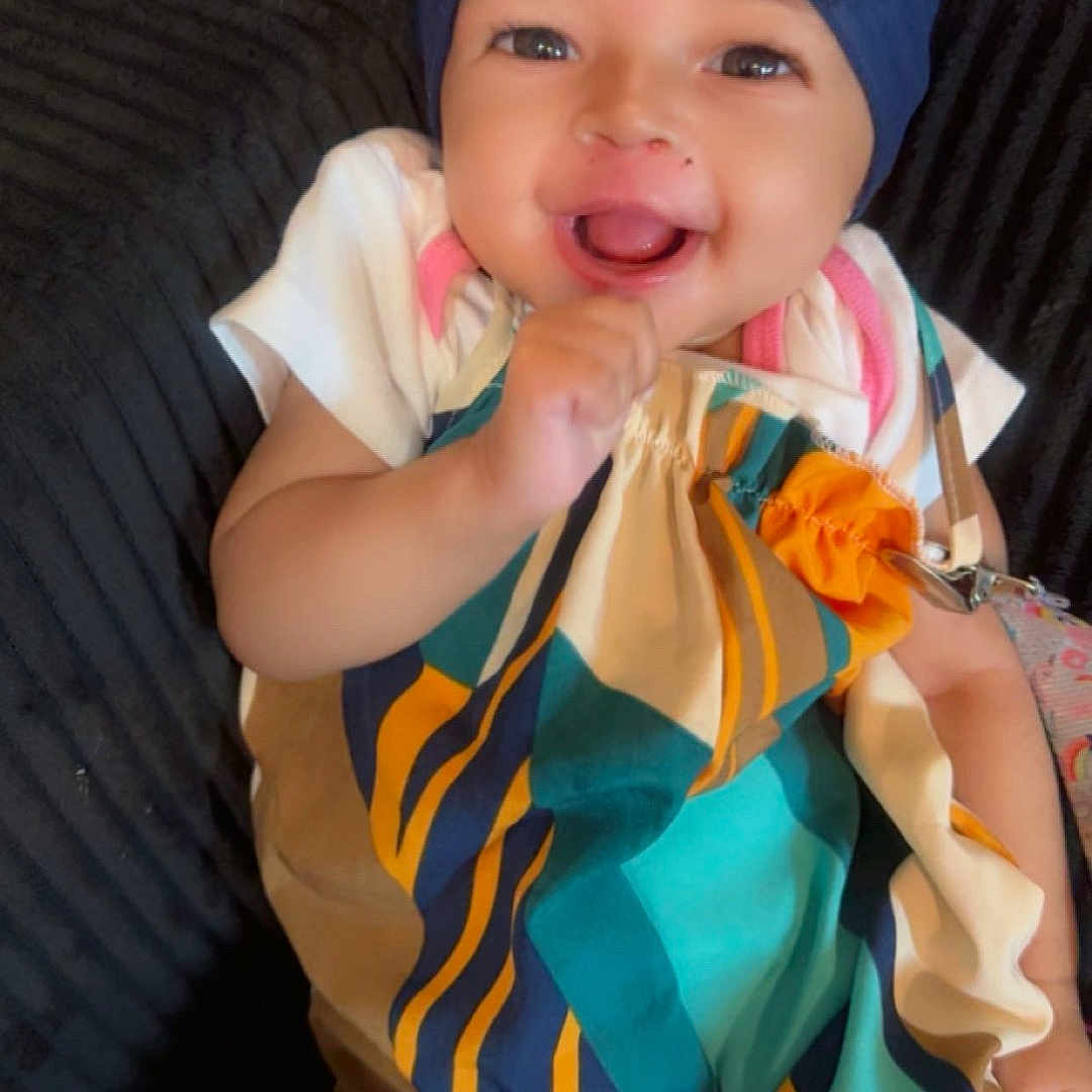 Ariyah joined the competition — help win amazing prizes! baby, child, infant, smiling, happy, portrait, fashion, bow, headband, colorful_clothing, dress, sitting, indoor, couch, textile, close_up, face, eyes, playful, photography