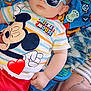 baby, child, sunglasses, mickey_mouse, colorful_clothing, blanket, tattoo, foot, hand, indoor, casual, relaxed, cute, person, portrait, toddler, striped_shirt, footwear, pacifier, blue
