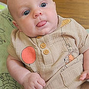 Cassius is registered to the contest to win money with this photo: baby, infant, tongue_out, blue_eyes, beige_outfit, balloon_print, dog_print, buttoned_shirt, cushion, patterned_fabric, wooden_floor, sofa, indoor, close_up, chubby_cheeks, cute, child, portrait, casual_clothing, relaxed