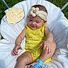baby, child, yellow_outfit, headband, flower, smile, sitting, blanket, outdoor, grass, wooden_sign, footwear, sandal, cute, infant, happy, person, skin, head, nature