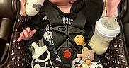 Jade joined the competition — help win amazing prizes! baby, infant, car_seat, pacifier, milk_bottle, black_clothing, white_clothing, cow_print, toy, wooden_beads, harness, cute, expression, pink_background, patterned_fabric, sitting, child, indoor, face, playful