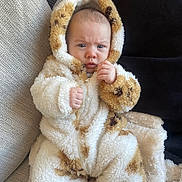 Atley is registered to the contest to win money with this photo: baby, child, couch, blanket, onesie, hood, fur, spot, clothing, indoor, person, face, expression, seated, hand, fingers, cozy, warm, texture, portrait