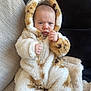 baby, child, couch, blanket, onesie, hood, fur, spot, clothing, indoor, person, face, expression, seated, hand, fingers, cozy, warm, texture, portrait