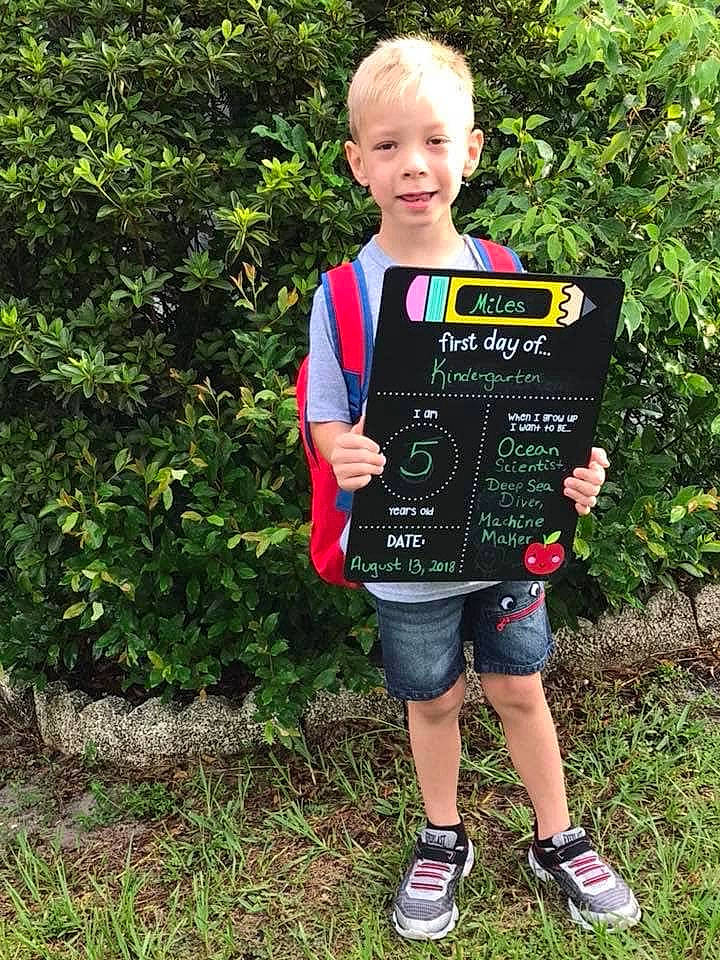 Miles is registered to the contest to win money with this photo: child, clothing, face, fun, garden, grass, groundcover, happy, joy, leisure, pattern, people_in_nature, person, plant, recreation, shorts, shrub, sleeve, smile, t_shirt