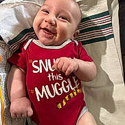 Luke joined the competition — help win amazing prizes! arm, baby, child, clothing, cute, expression, face, hand, happy, indoors, infant, lying_down, newborn, person, portrait, red_onesie, skin, smile, striped_cloth, text_on_clothing