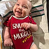 arm, baby, child, clothing, cute, expression, face, hand, happy, indoors, infant, lying_down, newborn, person, portrait, red_onesie, skin, smile, striped_cloth, text_on_clothing