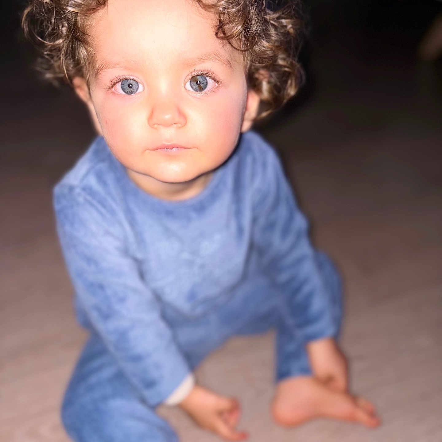 Lywann participe au concours pour gagner de l'argent avec cette photo : baby, blue_eyes, blurry_background, child, cozy, curly_hair, cute, expression, face, floor, indoor, infant, looking_at_camera, pajamas, person, portrait, sitting, soft_lighting, toddler, young_child