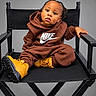 child, toddler, portrait, sitting, director_chair, brown_hoodie, nike, yellow_boots, braided_hair, black_chair, studio, indoor, fashion, streetwear, close_up, full_body, serious_expression, looking_at_camera, photography, safe