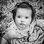 child, toddler, face, messy, black_and_white, portrait, curious, eyes, hair_clip, dress, sitting, outdoor, ground, texture, expression, young_child, person, innocence, closeup, monochrome