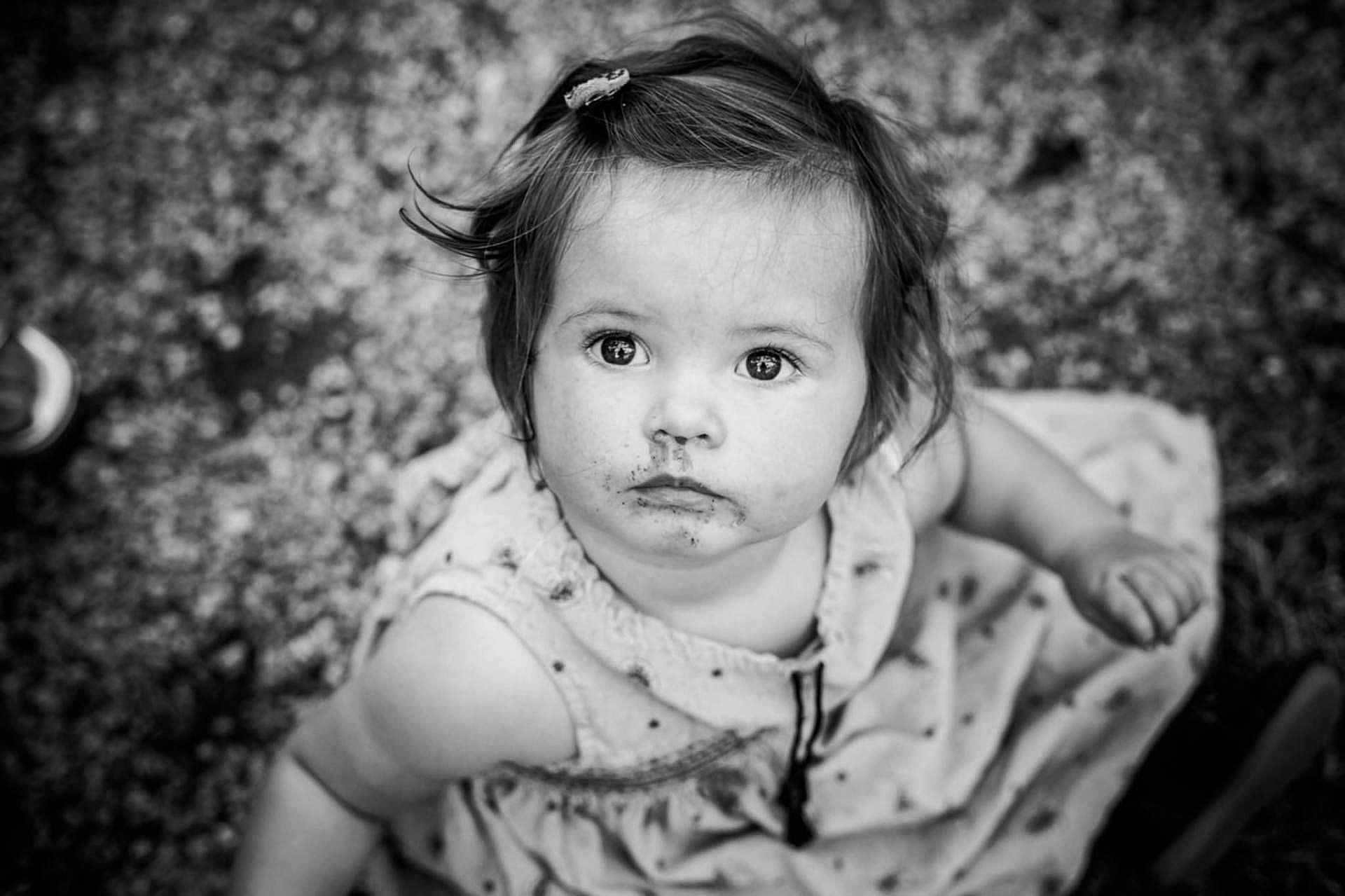 Thelma a rejoint le concours — aidez-le/la à gagner de superbes lots ! child, toddler, face, messy, black_and_white, portrait, curious, eyes, hair_clip, dress, sitting, outdoor, ground, texture, expression, young_child, person, innocence, closeup, monochrome
