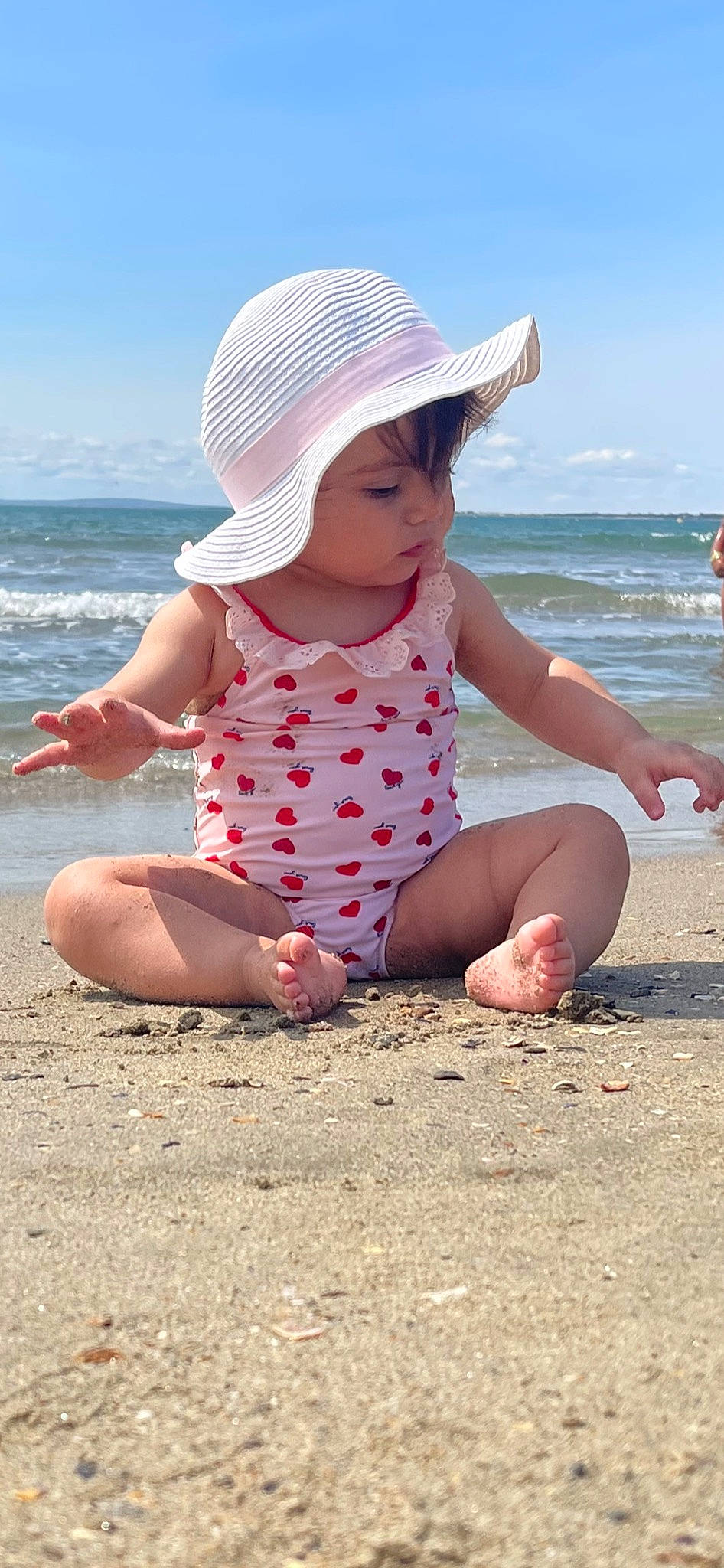 Mila participe au concours pour gagner de l'argent avec cette photo : baby_toddler_clothing, barefoot, beach, finger, foot, fun, happy, hat, human_body, leg, people_in_nature, people_on_beach, person, photograph, skin, sky, summer, sun_hat, thigh, toddler