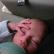 Oscar And Oliver is registered to the contest to win money with this photo: baby, bottle, feeding, infant, hand, face, sleepy, indoor, remote_control, sofa, clothing, newborn, peaceful, closeup, skin, head, person, resting, milk, young_child