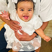 Diana joined the competition — help win amazing prizes! baby, child, white_dress, bows, smiling, tongue_out, waving_hand, adult_hands, white_shirt, happy, cute, portrait, indoor, holding, person, infant, fashion, close_up, joyful, playful