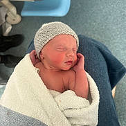 Louie is registered to the contest to win money with this photo: newborn, baby, infant, wrapped, towel, knitted_hat, sleeping, hand, person, lap, hospital, medical, floor, clothing, skin, face, peaceful, resting, indoors, soft