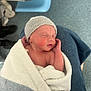newborn, baby, infant, wrapped, towel, knitted_hat, sleeping, hand, person, lap, hospital, medical, floor, clothing, skin, face, peaceful, resting, indoors, soft