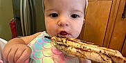Melody is registered to the contest to win money with this photo: apparel, baby, bow, cabinet, child, closeup, colorful_clothing, curious, cute, face, food, grilled_fish, hand, headband, indoors, infant, kitchen, mealtime, person, refrigerator