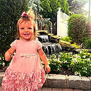 Melody joined the competition — help win amazing prizes! bow, child, cute, daylight, flowers, garden, girl, greenery, happy, nature, outdoor, pavement, pink_dress, plants, playful, portrait, smiling, toddler, walking, waterfall