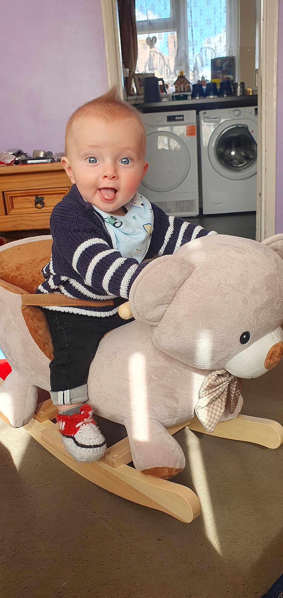 Lowen joined the competition — help win amazing prizes! baby, child, rocking_toy, plush_toy, bear, indoor, smiling, happy, knitted_shoes, striped_sweater, blue_eyes, carpet, wooden_rocker, baby_bib, furniture, laundry_machines, window, curtains, playful, home