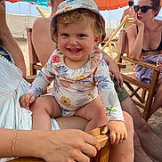 Margaux a rejoint le concours — aidez-le/la à gagner de superbes lots ! toddler, child, smiling, hat, floral_pattern, beach, umbrella, summer, sunlight, adult, sunglasses, chair, sand, outdoor, happy, family, vacation, casual, relaxing, people