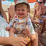 toddler, child, smiling, hat, floral_pattern, beach, umbrella, summer, sunlight, adult, sunglasses, chair, sand, outdoor, happy, family, vacation, casual, relaxing, people