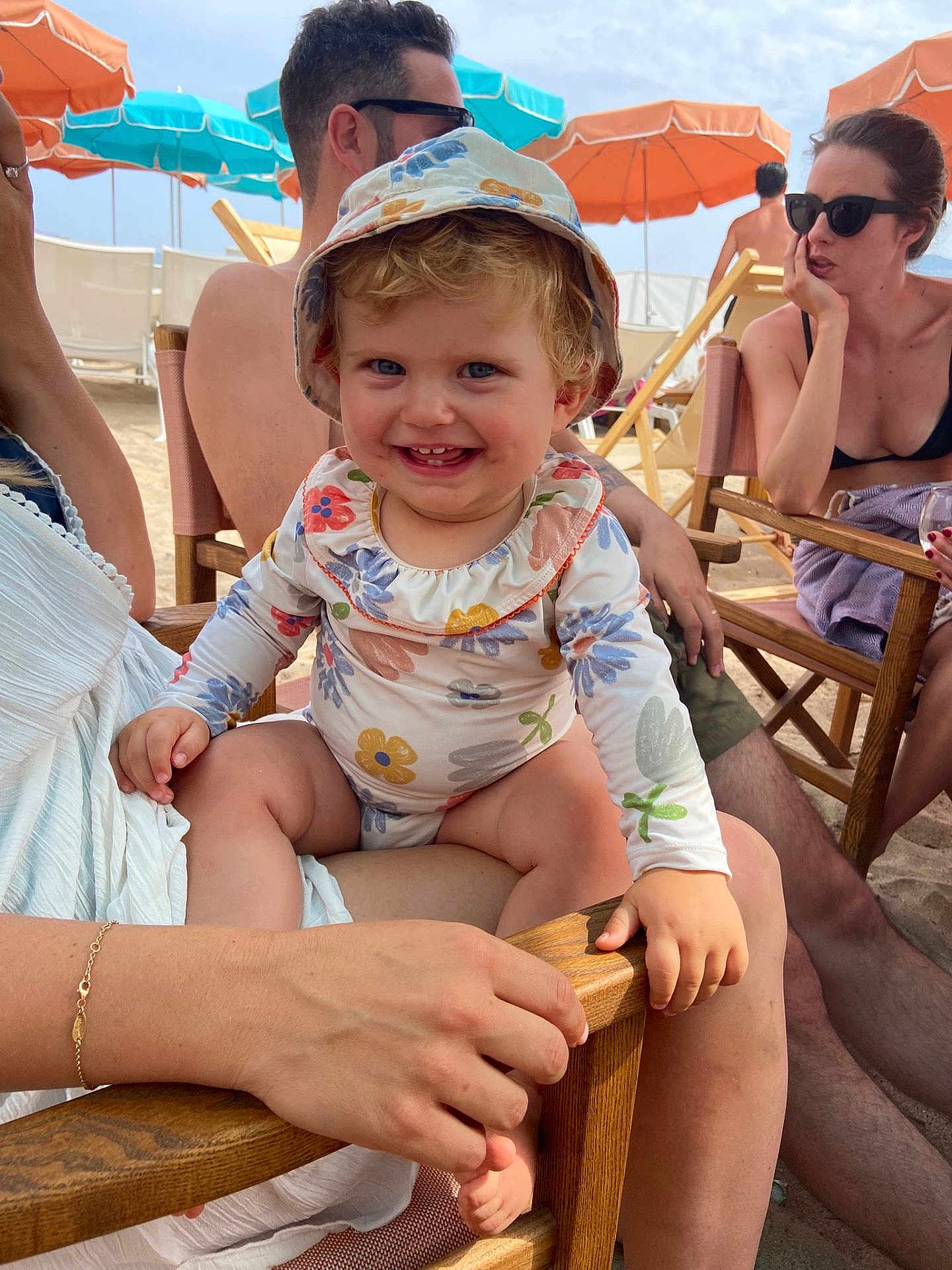 Margaux a rejoint le concours — aidez-le/la à gagner de superbes lots ! toddler, child, smiling, hat, floral_pattern, beach, umbrella, summer, sunlight, adult, sunglasses, chair, sand, outdoor, happy, family, vacation, casual, relaxing, people
