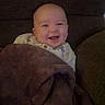 baby, blanket, brown, child, clothing, couch, cozy, eyes, face, happy, head, home, indoors, infant, laughing, mouth, phone_screenshot, portrait, seated, smiling