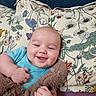 Layne is registered to the contest to win money with this photo: baby, blanket, blue_shirt, child, close_up, colorful, cozy, face, floral_cushion, hands, happy, home, indoors, infant, lying_down, portrait, smiling, soft_furnishings, stuffed_animal, teddy_bear