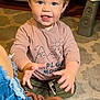 toddler, child, indoor, carpet, toy, shirt, pink_clothing, blue_eyes, happy, smiling, playing, hands, footwear, jeans, brown_shoes, furniture, wood_floor, hair, expression, person