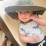 Miller joined the competition — help win amazing prizes! baby, child, hat, onesie, dinosaur_print, lying_down, indoor, person, feet, socks, shorts, fabric, smiling, face, hand, cute, infant, bed, light, casual_clothing