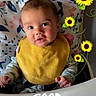 baby, child, high_chair, yellow_bib, face, expression, sunflowers, floral_pattern, cushion, indoor, person, smiling, morning, text_overlay, cute, infant, clothing, happy, portrait, feeding_time