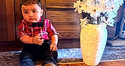 Rudra joined the competition — help win amazing prizes! toddler, child, indoor, wood_floor, wooden_furniture, red_shirt, bow_tie, black_pants, white_shoes, vase, white_flowers, curious_expression, sitting, portrait, decor, home_interior, floor_rug, plush, cute, young_child