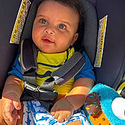 Amari joined the competition — help win amazing prizes! baby, car_seat, blue_eyes, yellow_shirt, blue_shorts, plush_toy, sunlight, safety_harness, child, infant, cute, smiling, curly_hair, seat_belt, colorful, indoor, portrait, happy, skin, clothing