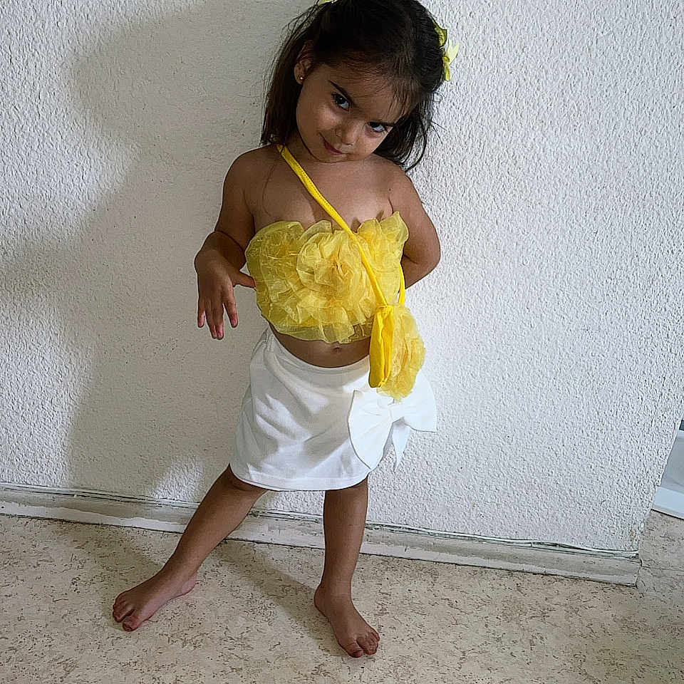 Layana participe au concours pour gagner de l'argent avec cette photo : attitude, barefoot, casual, child, cute, fashion, floor, girl, hair_bow, indoor, person, playful, portrait, posing, shadow, smile, standing, wall, white_skirt, yellow_top