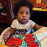 booth, casual, child, colorful_cloth, curly_hair, cute, expression, food_place, furniture, indoor, lighting, people, person, restaurant, seated, spiderman, table, toddler, white_tshirt, young