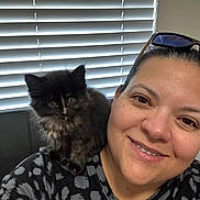 Mocha is registered to the contest to win money with this photo: person, smile, kitten, black_cat, pet, shoulder, indoor, window_blinds, glasses, happy, cute, fur, face, casual_clothing, closeup, animal, companion, friendly, cozy, portrait