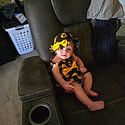 Briar is registered to the contest to win money with this photo: baby, child, hat, sunflower, outfit, recliner, chair, clothing, home_interior, furniture, floor, laundry_basket, curious, smile, barefoot, sitting, infant, indoor, person, cute