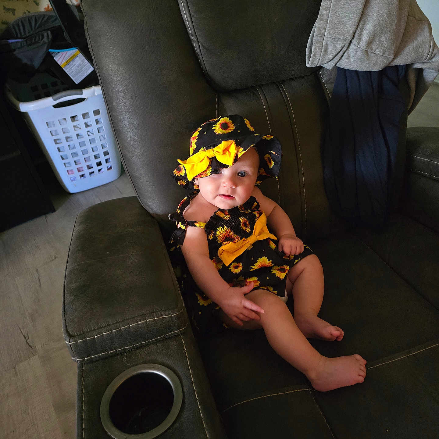 Briar is registered to the contest to win money with this photo: baby, child, hat, sunflower, outfit, recliner, chair, clothing, home_interior, furniture, floor, laundry_basket, curious, smile, barefoot, sitting, infant, indoor, person, cute