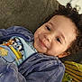Legend is registered to the contest to win money with this photo: child, toddler, smile, curly_hair, blue_jacket, cartoon_tshirt, couch, pillow, indoor, face, happy, person, portrait, clothing, cozy, young_child, relaxing, casual, cute, home